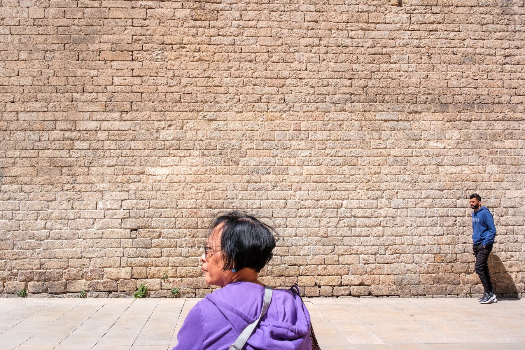 Street photograph in Barcelona with figures layered against a sunlit stone wall